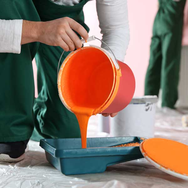 man pouring orange paint from a bucket into a paint tray