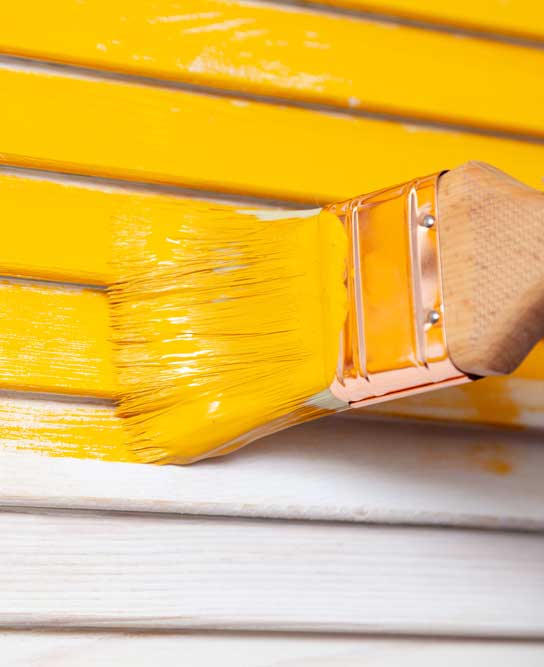 paint brush putting yellow paint on exterior siding